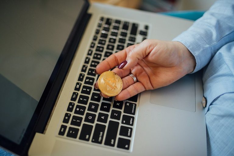 Close-up of a Bitcoin physical coin in a womans hand and a laptop on her lap