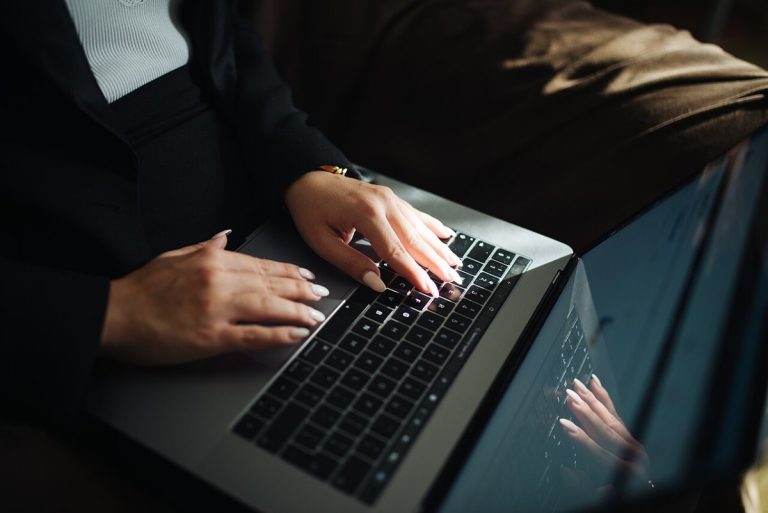 Woman with long nails typing on a laptop keyboard